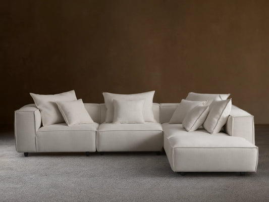 Coburn Five-Piece Sectional, L-shaped, upholstered in light grey fabric, with many soft accent pillows, on a wood floor.