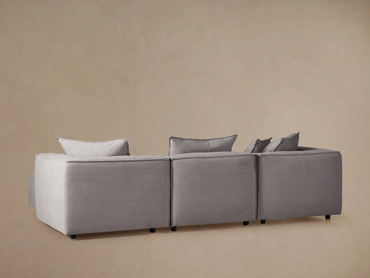 Light gray Coburn Four-Piece Sectional, L-shaped, with plush cushions, visible stitching, and loose back pillows.