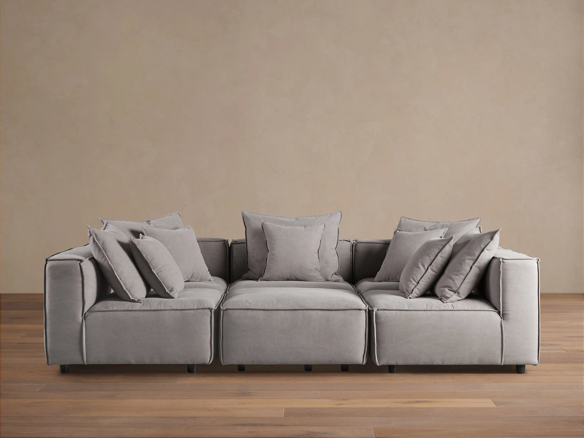 Gray Coburn Six-Piece Pit Sectional on wooden floor, with plush back and seat cushions and multiple pillows, set against a neutral wall.