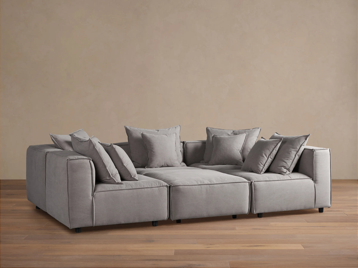 Gray Coburn Six-Piece Pit Sectional on wooden floor, with plush back and seat cushions and multiple pillows, set against a neutral wall.