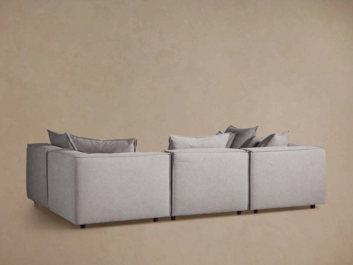 Coburn Six-Piece Pit Sectional in a neutral gray fabric with plush back pillows, block design, and wooden floor setting.