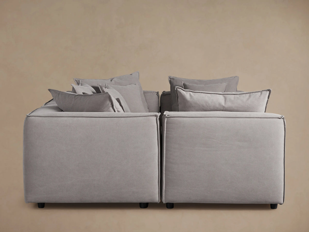 Coburn Six-Piece Pit Sectional in light gray fabric, arranged in a U-shape, showcasing abundant back pillows and plush cushions against a beige background.