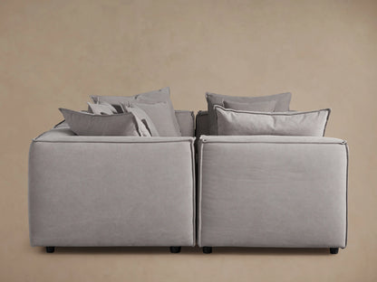 Coburn Six-Piece Pit Sectional in light gray fabric, arranged in a U-shape, showcasing abundant back pillows and plush cushions against a beige background.