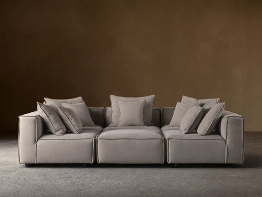 Gray Coburn Six-Piece Pit Sectional on wooden floor, with plush back and seat cushions and multiple pillows, set against a neutral wall.