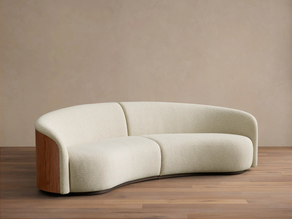 Front view of the curved cream Caden Two-Piece Sectional with walnut wood veneer end panels.