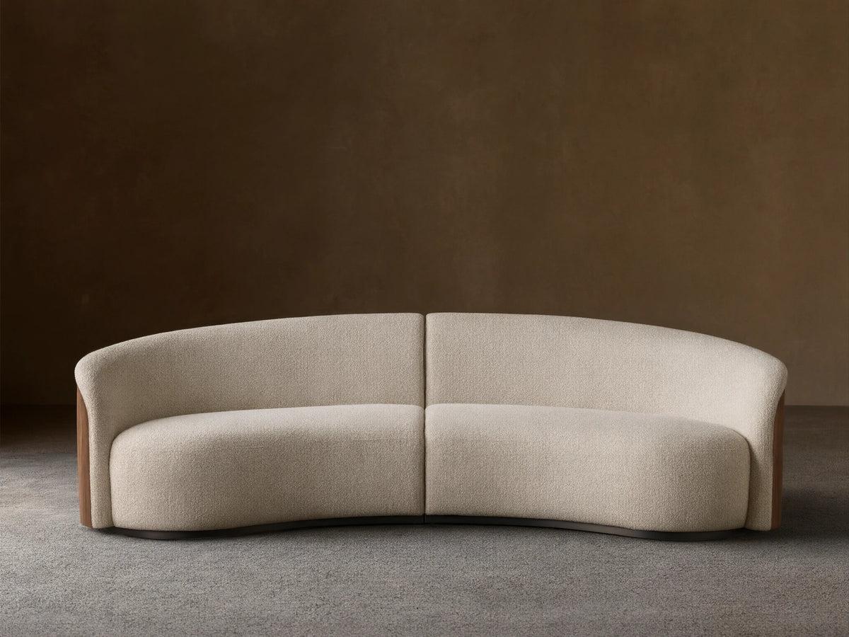 Front view of the curved Caden Two-Piece Sectional, upholstered in cream textured fabric with dark walnut wood veneer sides.