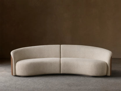 Front view of the curved Caden Two-Piece Sectional, upholstered in cream textured fabric with dark walnut wood veneer sides.