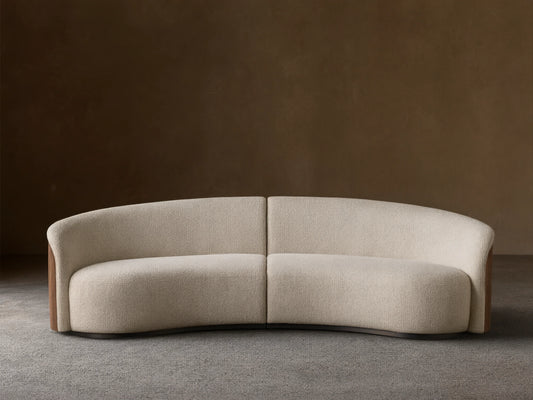 Front view of the curved Caden Two-Piece Sectional, upholstered in cream textured fabric with dark walnut wood veneer sides.