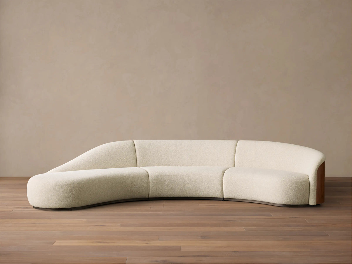 Front view of the cream Caden Three-Piece Bumper Sectional with a curved design and walnut veneer end panel.