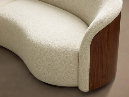 Close-up of the curved light beige textured upholstery and dark walnut wood panel on the Caden Three-Piece Bumper Sectional.