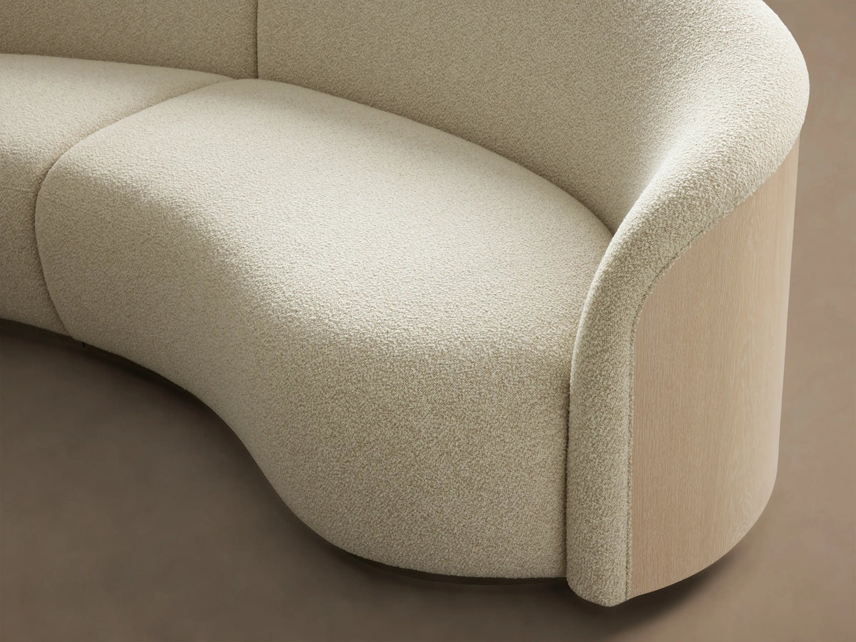 Close-up of the cream textured fabric and sand oak wood paneling of the Caden Three-Piece Bumper Sectional™.