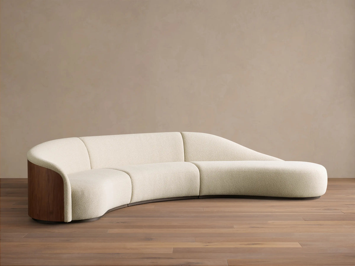 Front view of the cream Caden Three-Piece Bumper Sectional, with a curved design, walnut wood side panel, and chaise bumper.