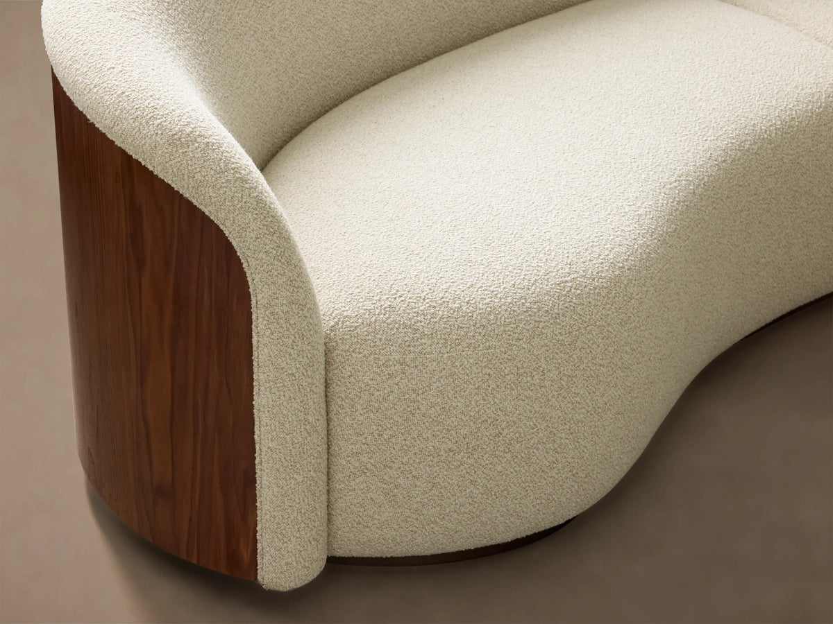 Front view of a cream Caden Three-Piece Bumper Sectional, featuring a curved design and a walnut veneer panel on the left end.