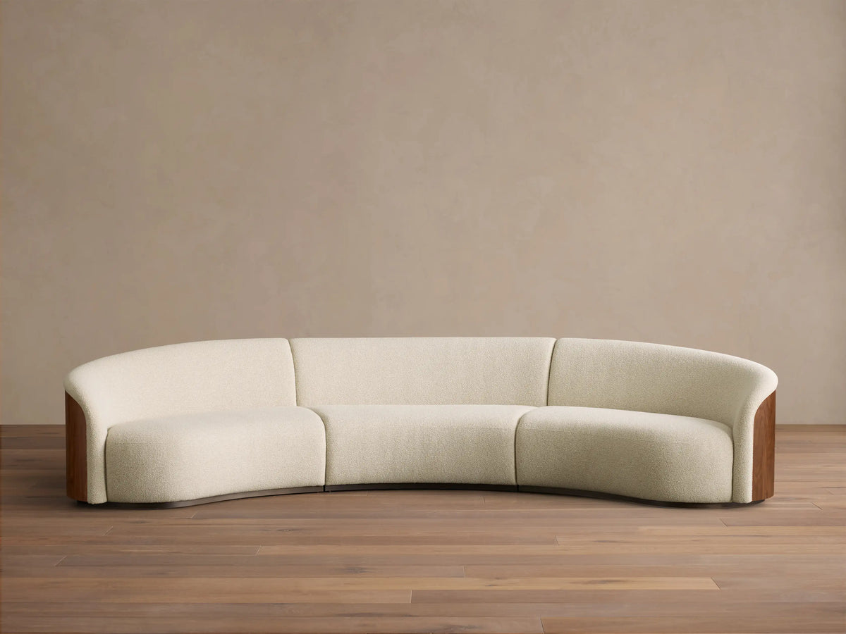 Front view of an off-white Caden Three-Piece Sectional with a curved design, upholstered in textured fabric and dark walnut veneer side panels.