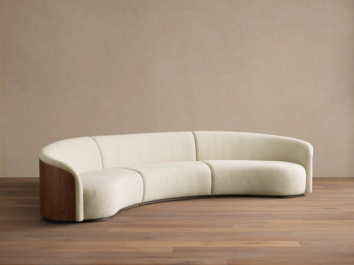 Rear view of the curved Caden Three-Piece Sectional with rich walnut veneer paneling and a cream upholstered top edge.