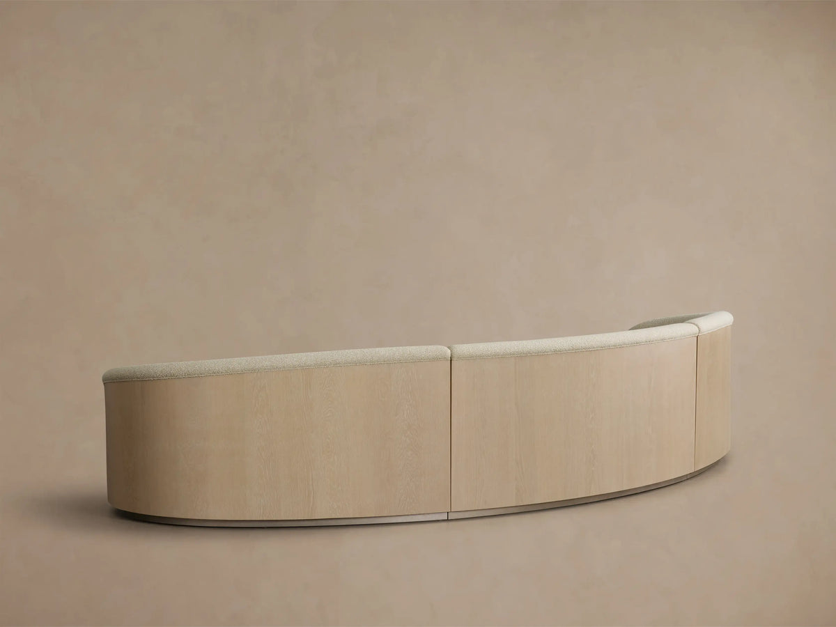 Rear view of the sand Caden Three-Piece Sectional, showing its curved oak veneer panels and light fabric top trim.