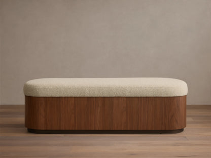 Front view of the Caden Storage Bench, featuring a dark walnut veneer base, an antique bronze plinth, and a light cream upholstered top.