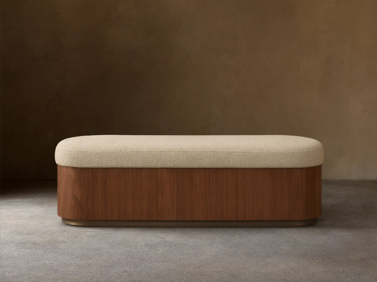 Front view of the Caden Storage Bench, featuring a dark walnut veneer base, an antique bronze plinth, and a light cream upholstered top.