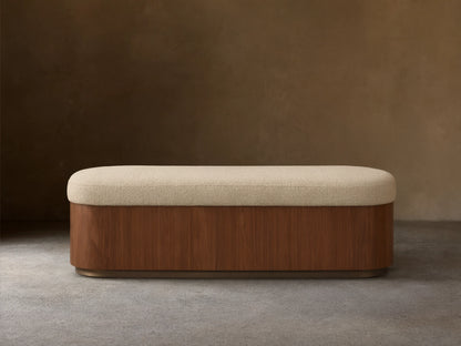 Front view of the Caden Storage Bench, featuring a dark walnut veneer base, an antique bronze plinth, and a light cream upholstered top.