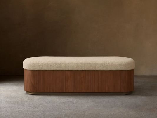 Front view of the Caden Storage Bench, featuring a dark walnut veneer base, an antique bronze plinth, and a light cream upholstered top.