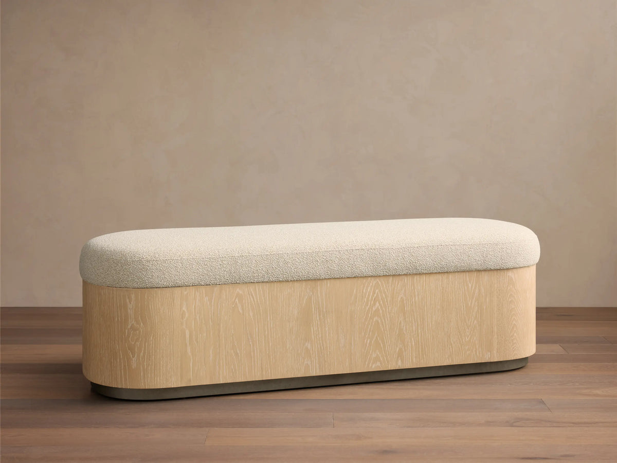 Front view of the Caden Storage Bench, featuring a cream textured cushion and an elongated sand oak veneer base with a dark gray plinth.