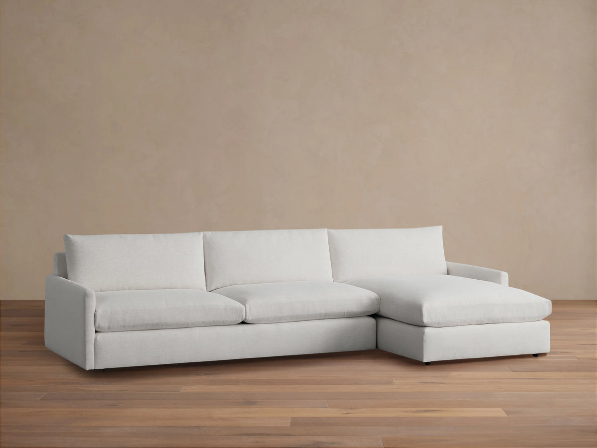 Alt text: Kipton Two-Piece Chaise Sectional in light fabric, featuring three-seat cushions and a right-side chaise, on a wooden floor.