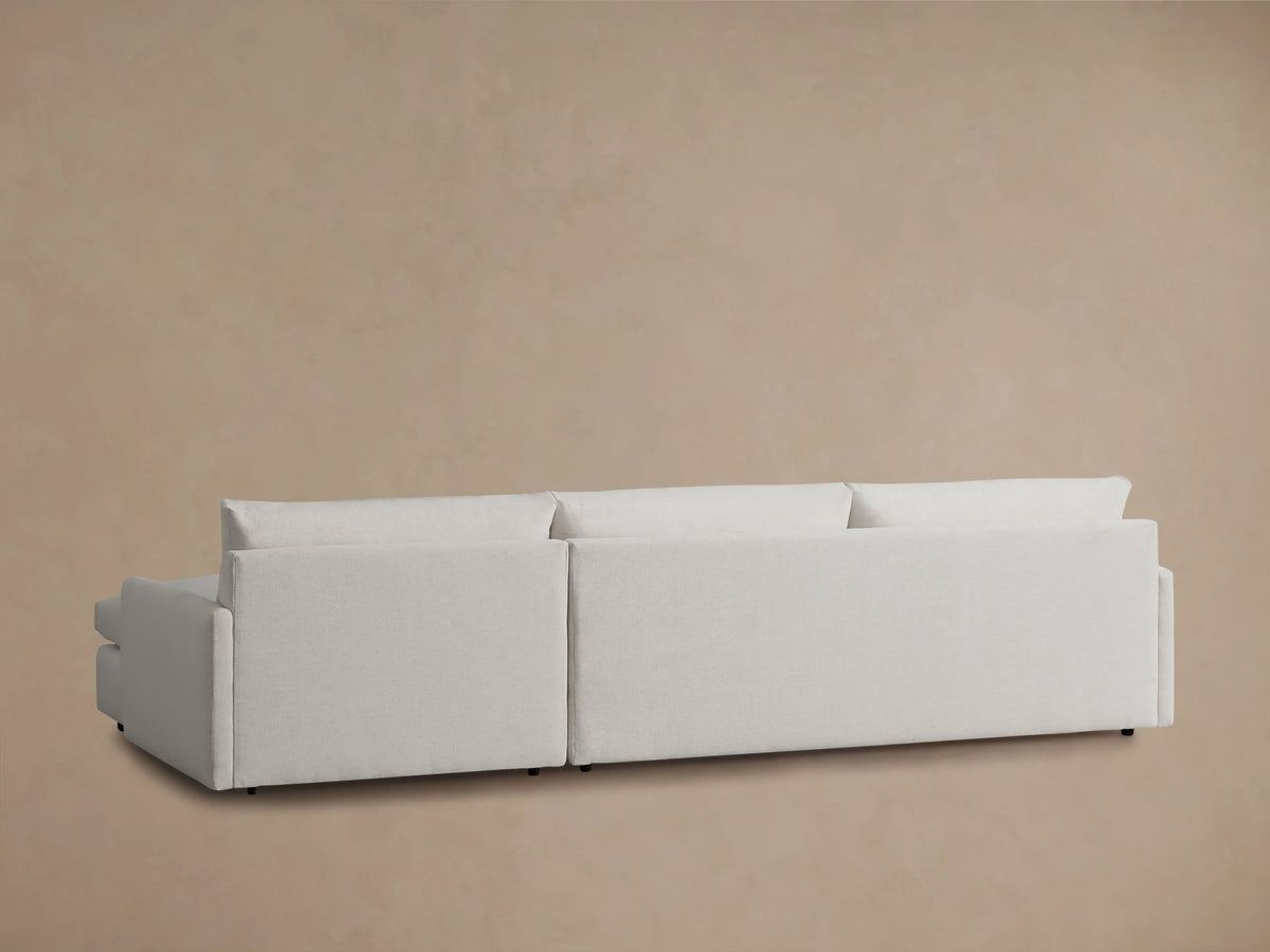 The image shows the back view of the Kipton Two-Piece Chaise Sectional in a light fabric, emphasizing its modern, rectangular shape against a neutral background.