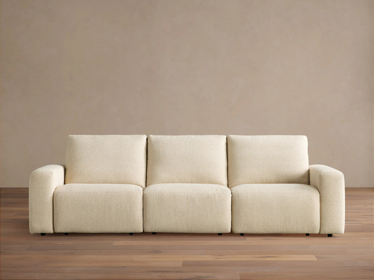Brennan Three-Piece Motion Sofa, light cream textured fabric, modern design with blocky arms & cushions, on wood floor.