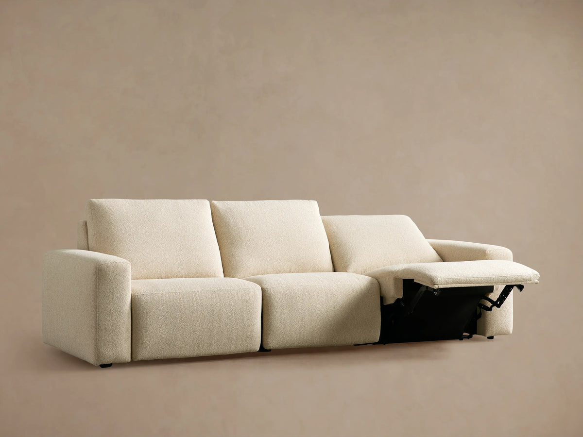 Brennan Three-Piece Motion Sofa in light beige fabric, with two footrests extended, against a plain tan wall.