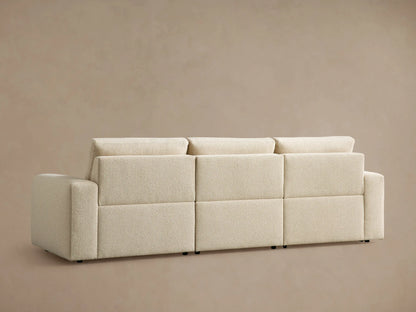 Brennan Three-Piece Motion Sofa in textured off-white fabric. Right seat reclined with footrest extended, against a light brown wall.