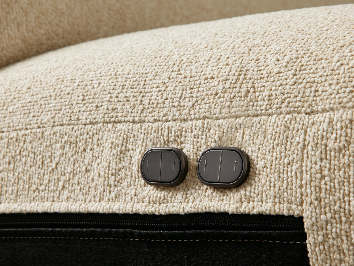 Close-up of a light beige, textured Brennan Motion Sectional's seat cushions with a footrest extended forward.