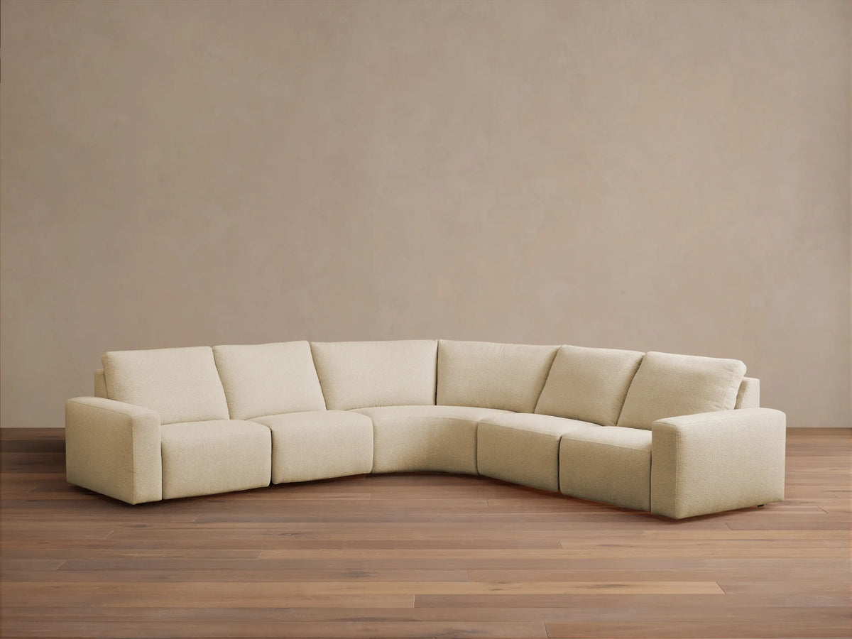 Brennan Five-Piece Motion Corner Sectional: light beige L-shaped sofa with curved corner against a neutral wall, wood floor.