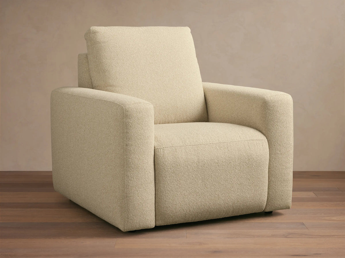 Brennan Motion Recliner in light beige textured fabric, an upright armchair with wide arms, on a wooden floor.