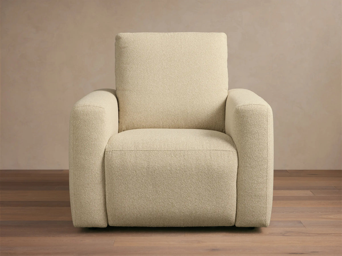 Brennan Motion Recliner in light beige textured fabric, an upright armchair with wide arms, on a wooden floor.