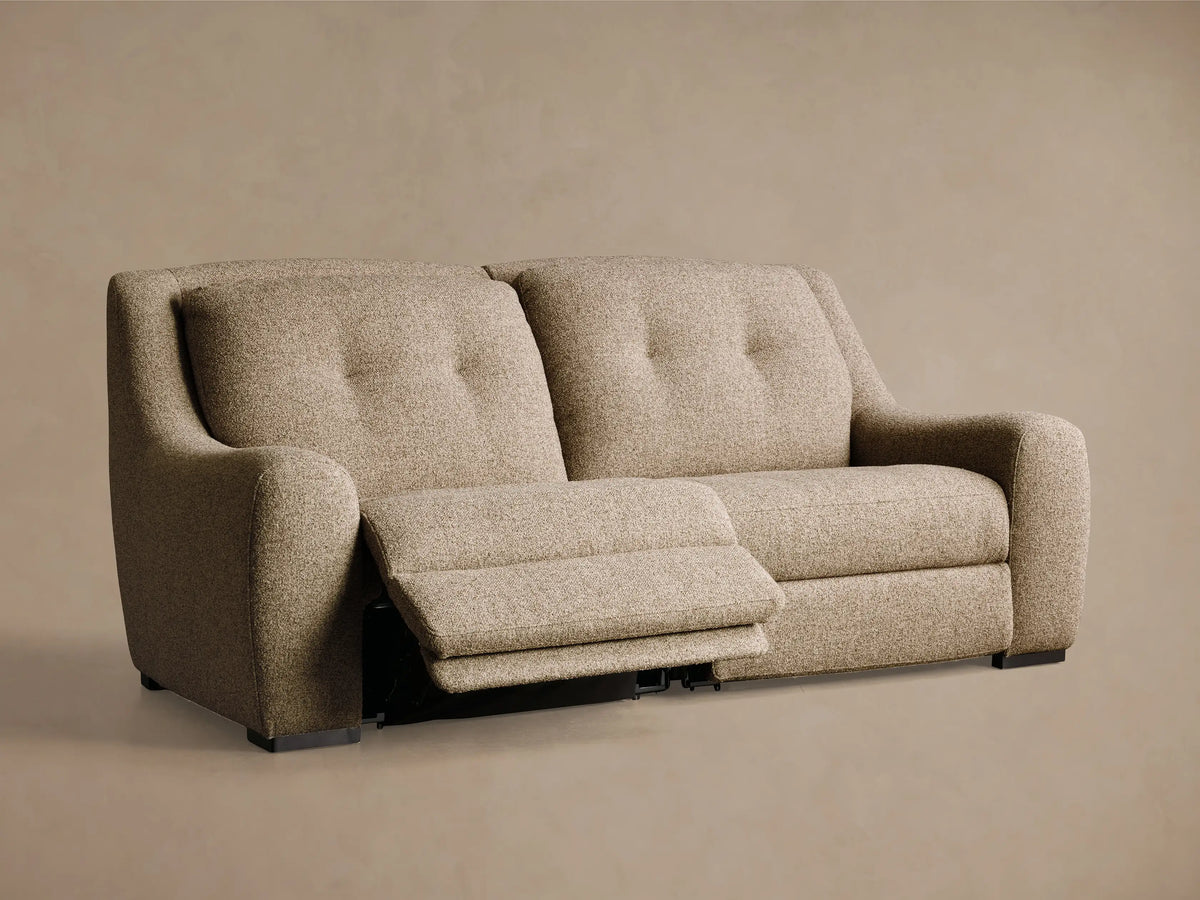 Front-angled view of a light brown textured Perry Two-Piece Motion Sofa with tufted back cushions and the right footrest extended.
