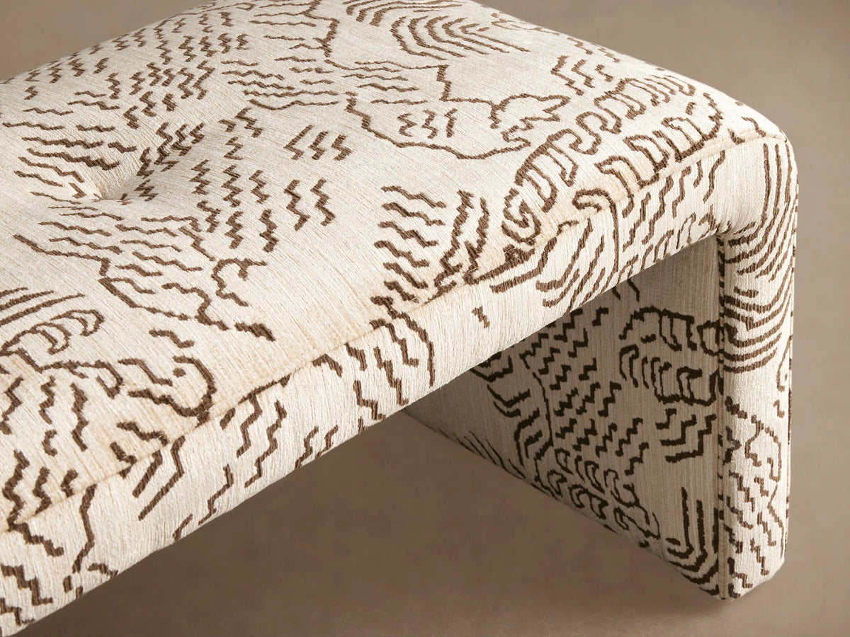 Ryan Bench: curved, cream upholstered bench with a dark brown abstract wavy pattern, on a wooden floor.