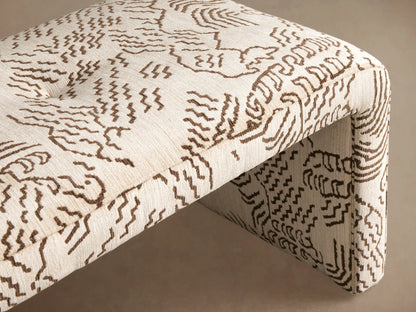 Ryan Bench: curved, cream upholstered bench with a dark brown abstract wavy pattern, on a wooden floor.