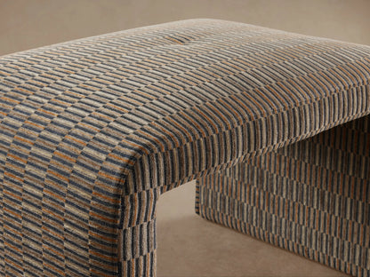 Ryan Ottoman with a woven, textured fabric in a multi-tonal pattern of brown and gray hues, arched top, and straight sides on hardwood floor background.