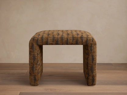 Front view of the brown upholstered Ryan Petite Ottoman with a dark geometric pattern and rounded edges.