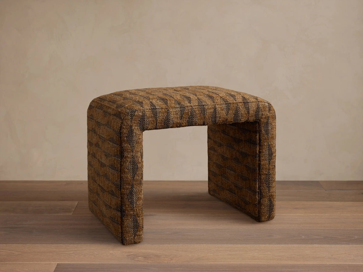Front view of the brown upholstered Ryan Petite Ottoman with a dark geometric pattern and rounded edges.