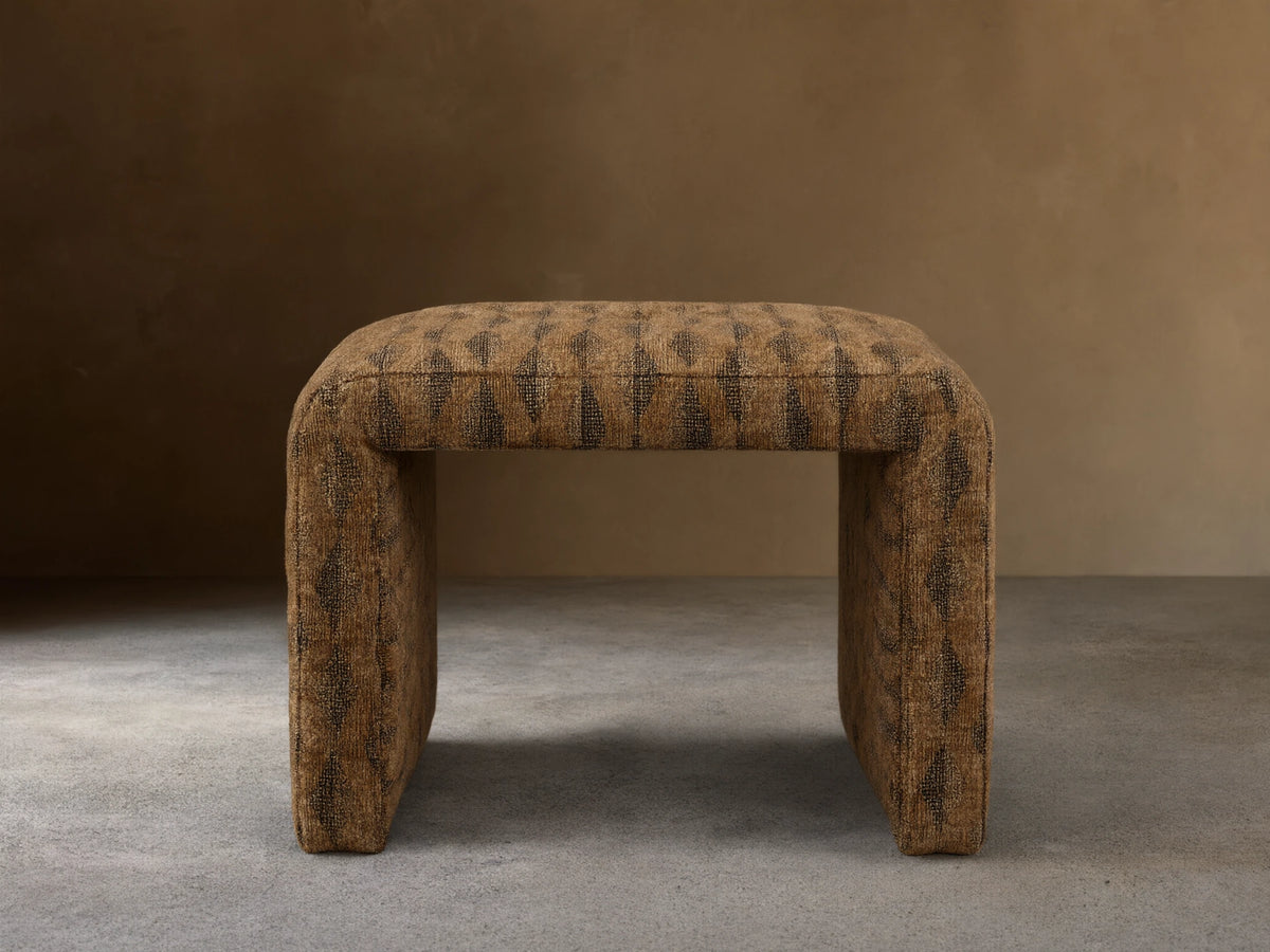 Front view of the brown upholstered Ryan Petite Ottoman with a dark geometric pattern and rounded edges.