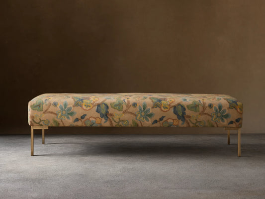Rectangular Tilton Bench upholstered in tan floral fabric with blue, green, yellow pattern, on slender gold legs.
