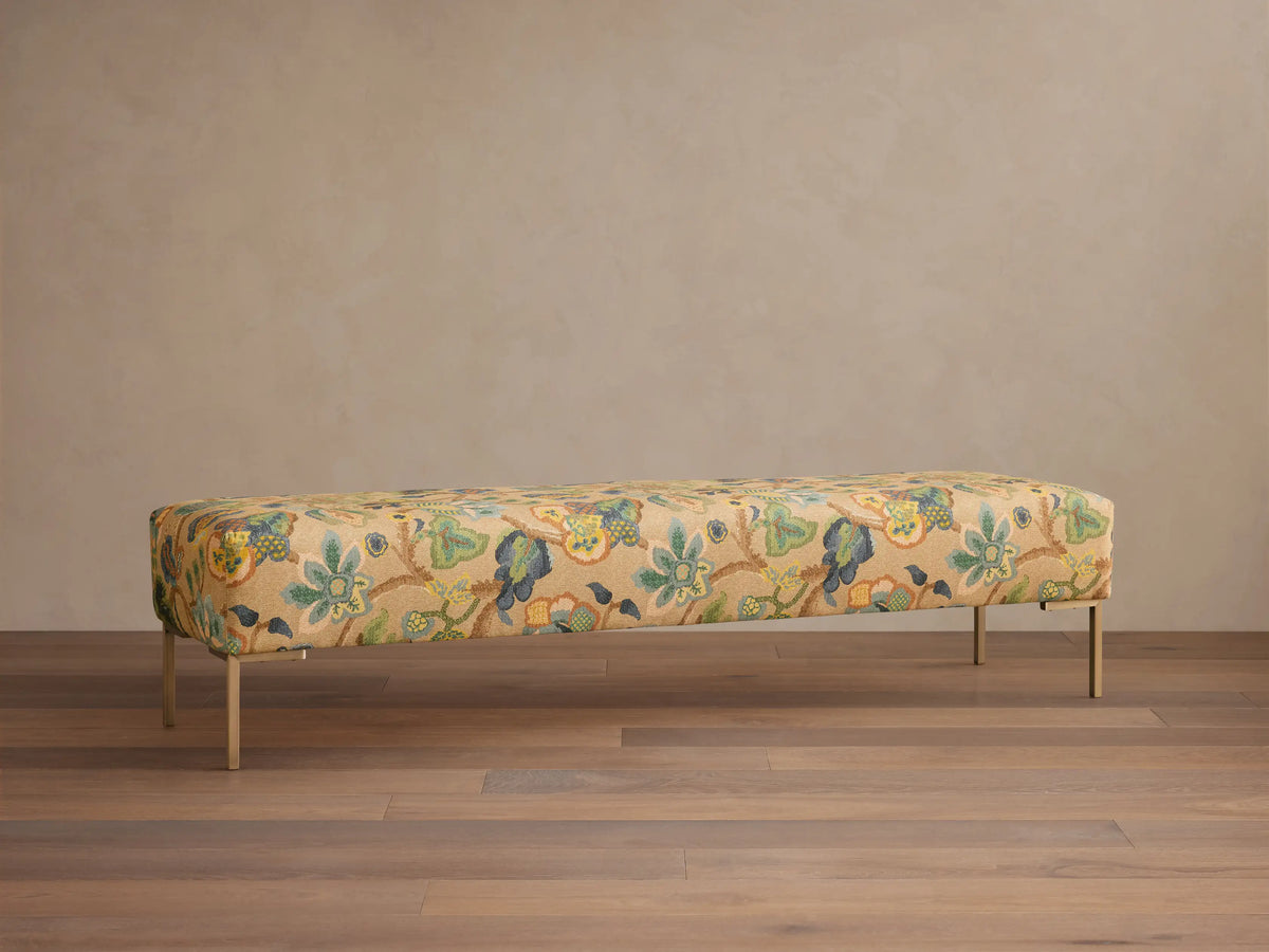 Front view of the Tilton Bench, a rectangular upholstered bench with a blue, brown, green botanical pattern and slender gold legs.