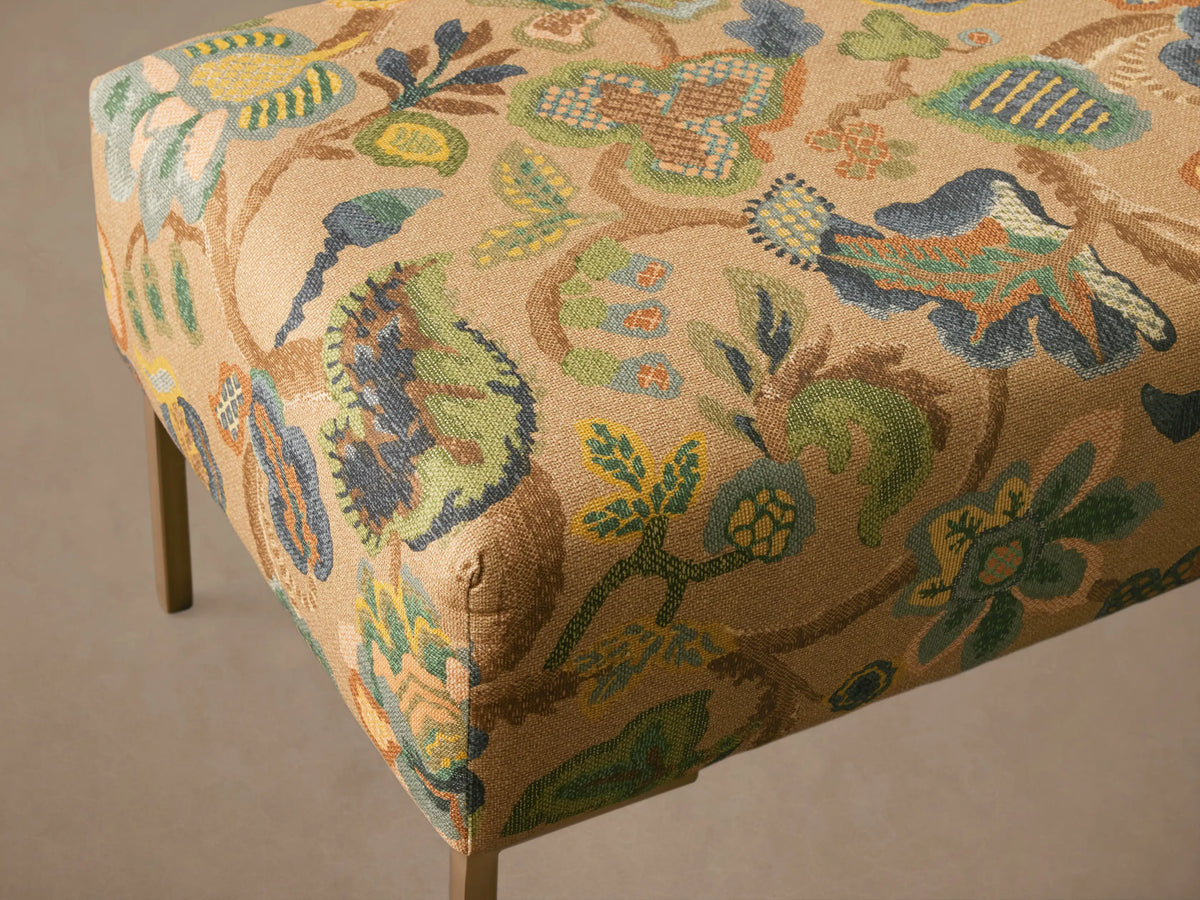 Tilton Bench, upholstered in beige fabric with vibrant green, blue, and yellow floral pattern, on slim gold metal legs.