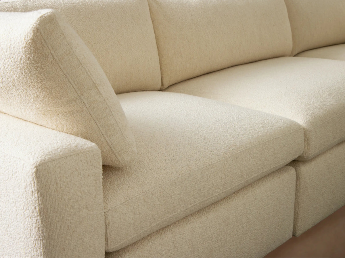 Front view of Beale Three-Piece Modular Sofa in textured cream fabric, with two accent pillows, against a brown wall & wood floor.