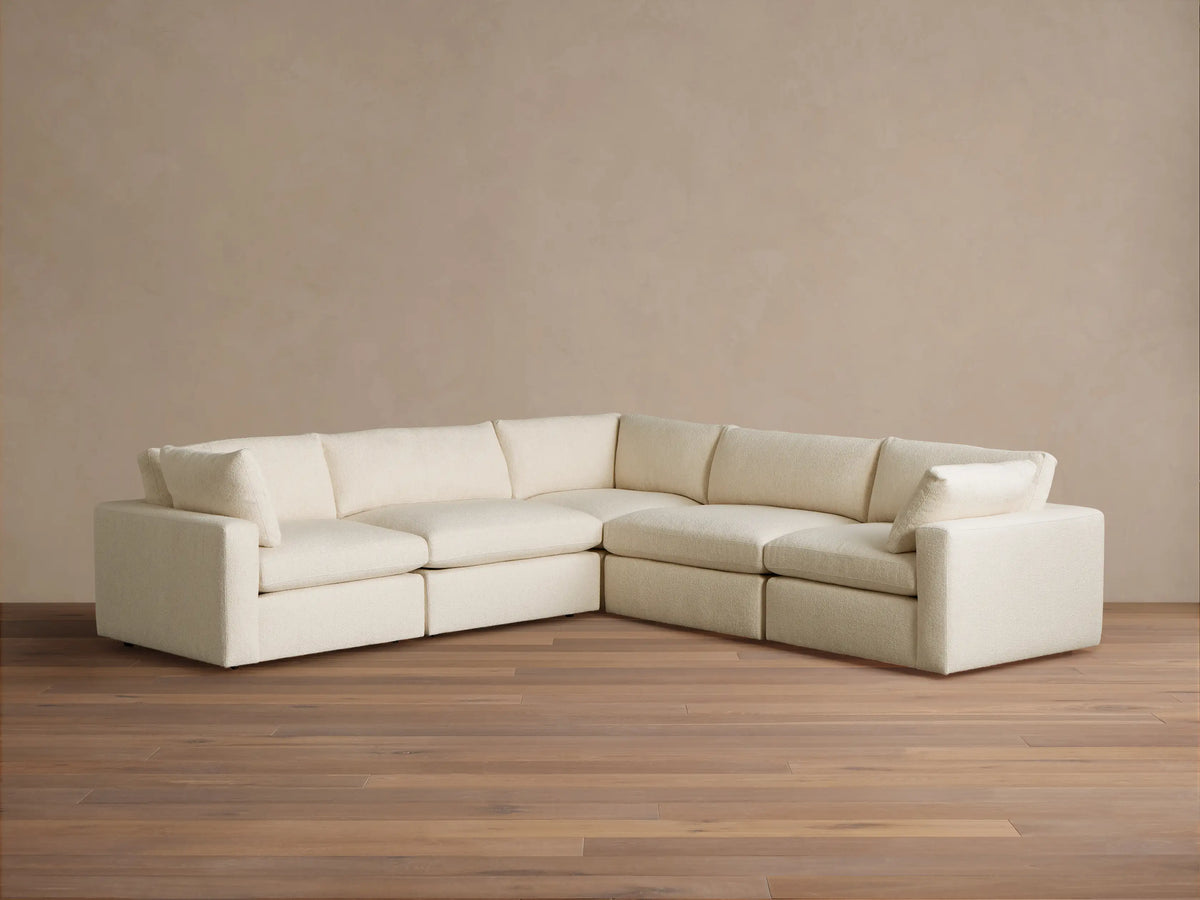 Creamy white Beale Five-Piece Corner Sectional sofa, L-shaped, on a wood floor against a beige wall. Plush textured fabric.