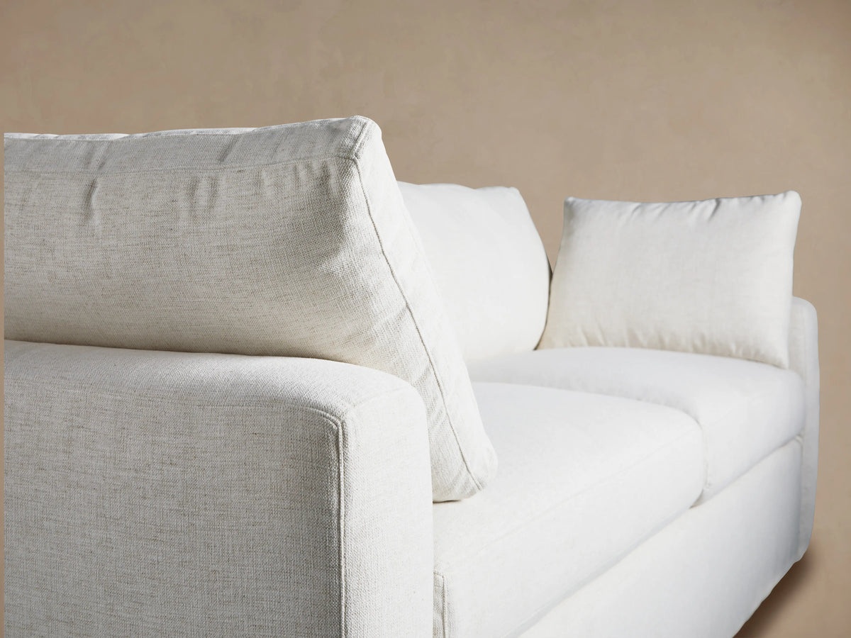 Light off-white Beale Sofa with two seat and back cushions, two arm pillows. Front-facing on a wooden floor against a tan wall.