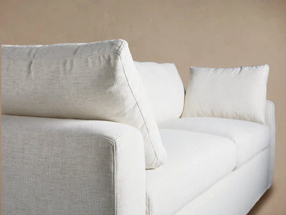 Light off-white Beale Sofa with two seat and back cushions, two arm pillows. Front-facing on a wooden floor against a tan wall.