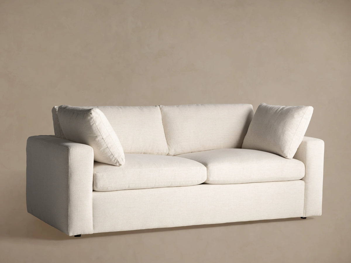 Beale Sofa, front view. Relaxed-style, light beige textured fabric. Two seat, two back cushions, two matching pillows on arms.