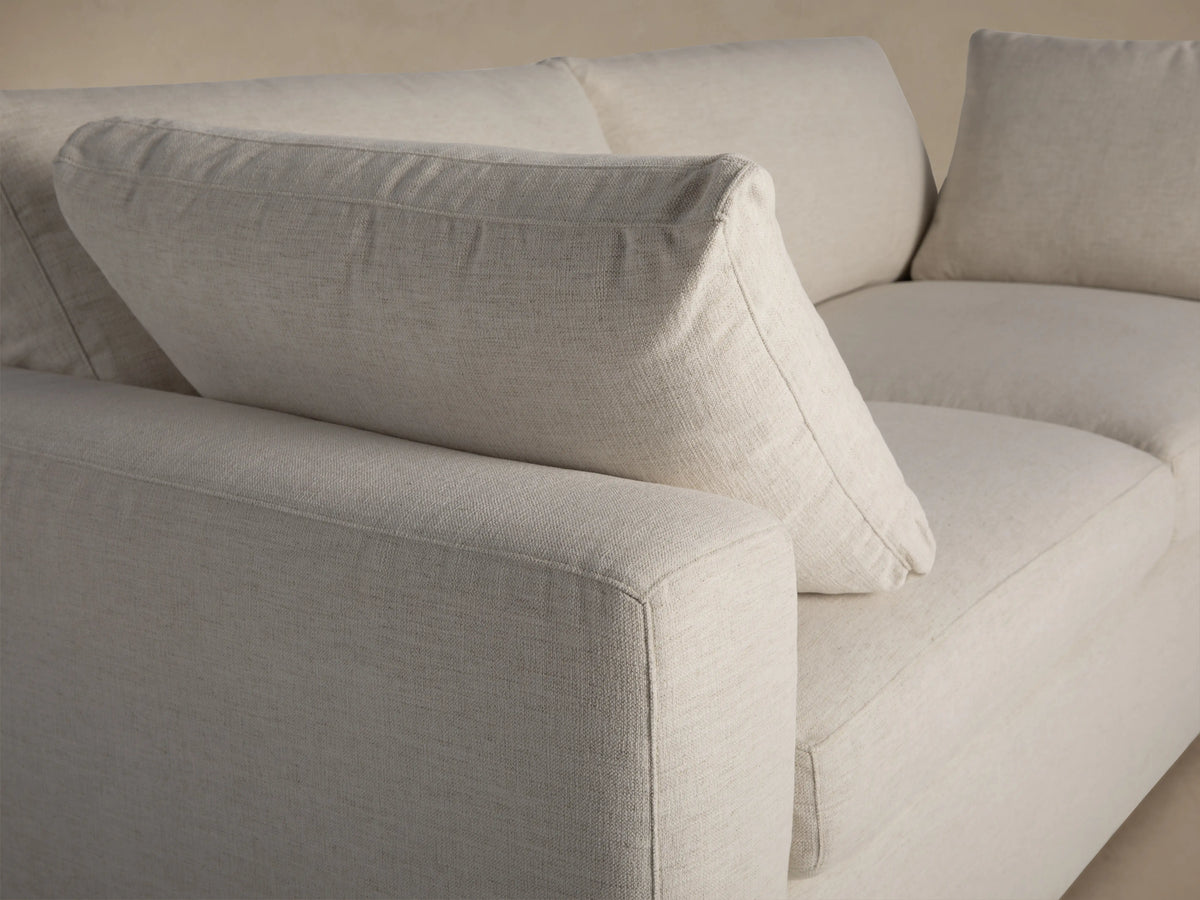 Beale Sofa: Relaxed, light cream two-seater sofa with wide square arms and plump, inviting cushions against a warm taupe wall.